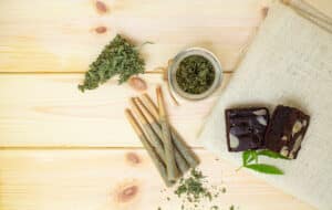 Pre-Roll marijuana joints and cake brownies with cannabis buds in a clear glass jar laying on the sackcloth