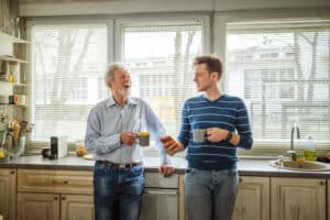Father and adult son enjoying a morning coffee and bonding over a cheerful conversation, creating a strong family relationship while standing in a bright kitchen